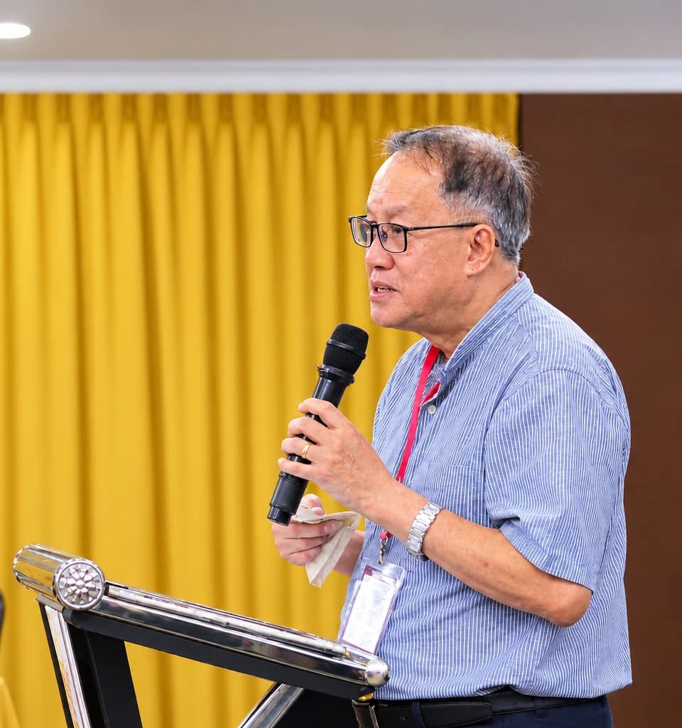 Mathew speaking into a microphone at the podium during a fellowship gathering